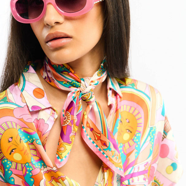 Baigné dans un univers fantasmagorique et hallucinogène, ENCHANTERED se pare en son centre d'un œil façon pentacle autour duquel quatre soleils aux visages poupons viennent se dessiner. Dans cette même veine, le reste du foulard raconte un monde à part, à la frontière de l'inconscient et d'un imaginaire débridé et coloré, sur fond de larges rayures empruntées à l'esthétique des années 70. Décliné en deux couleurs, ENCHANTERED est ici dans sa version rose et se révèle dans des tons turquoise, jaunes, oranges